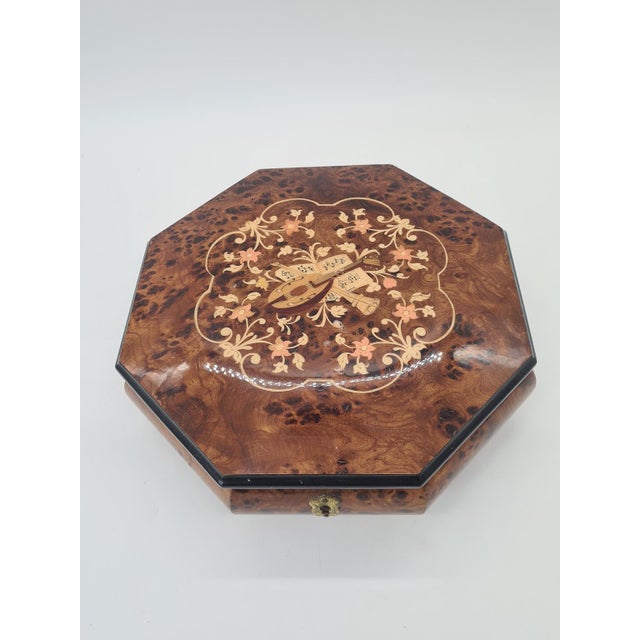 An elegant, decorative music box made of burl veneer. The lid is adorned with intricate marquetry depicting musical...