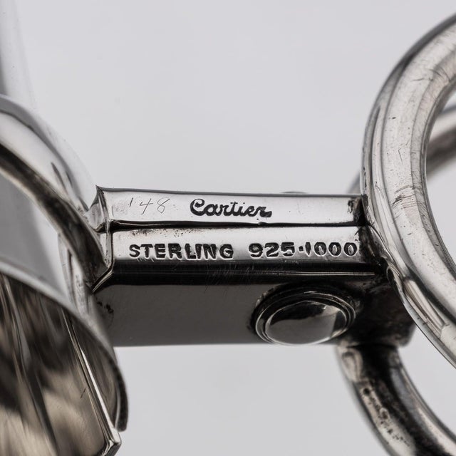 A 20th century american solid silver wine bottle holder by cartier. Of rounded form with pivot action twin scroll handles....