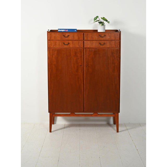 1950s mahogany cabinet with four upper drawers, hinged doors, and slender legs with a distinctive design. Scandinavian...