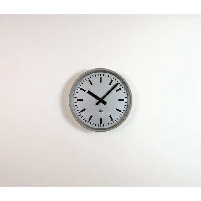 TCW post office wall clock was made in Netherlands during the 1960s. It features a grey iron frame, a metal dial, an...
