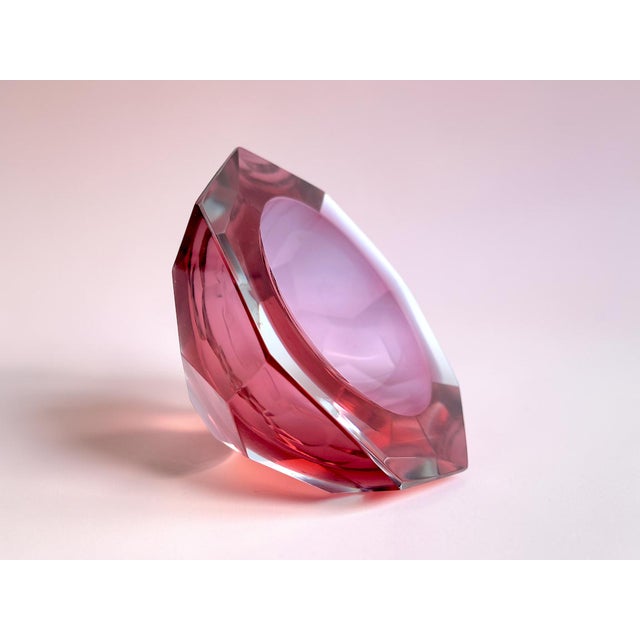 The body of the ashtray is made of clear glass, while the interior is cranberry pink. The contrast between the clear and...