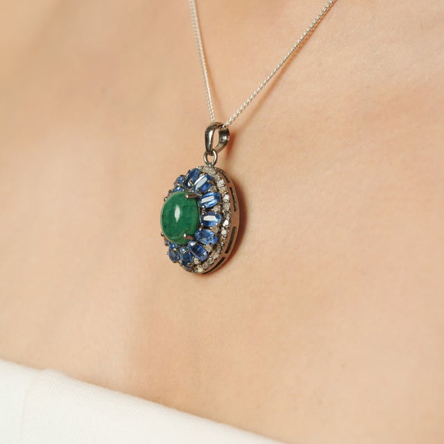 This elegant pendant is crafted in 925 sterling silver and features a striking natural Glass Filled-Emerald cabochon at...