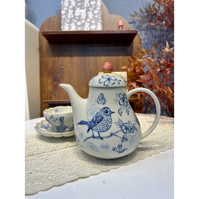 A fresh, vintage-style blue-and-white tea set featuring floral and bird motifs, complete with a teapot, a cup, and a saucer.