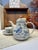 A fresh, vintage-style blue-and-white tea set featuring floral and bird motifs, complete with a teapot, a cup, and a saucer.