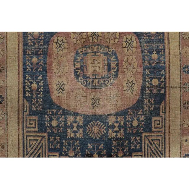 Hand-knotted in wool and originating circa 1870-1879, this 6x10 antique Khotan rug features two geometric medallions on a...