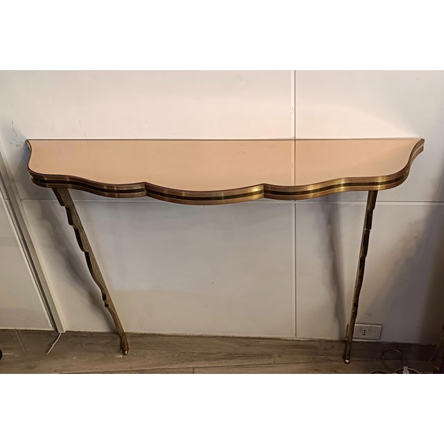 An elegant Italian wall-mounted console table from the 1940s, crafted from solid brass with a pink mirrored glass top,...