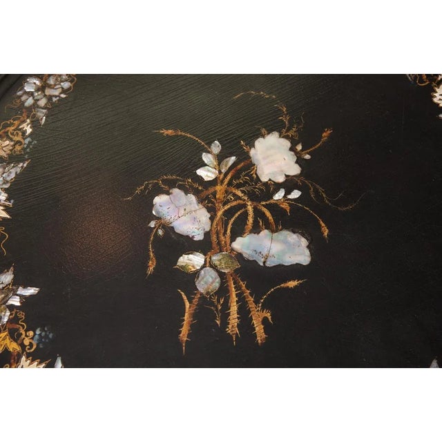 English papier mache and mother of pearl inlayed top on a painted black traditional three leg base. top is further...