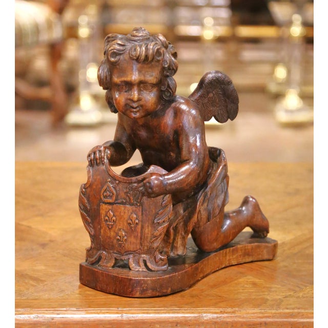 Hand-carved in France circa 1780, this exceptional antique oak sculpture depicts a kneeling winged putto presenting a...