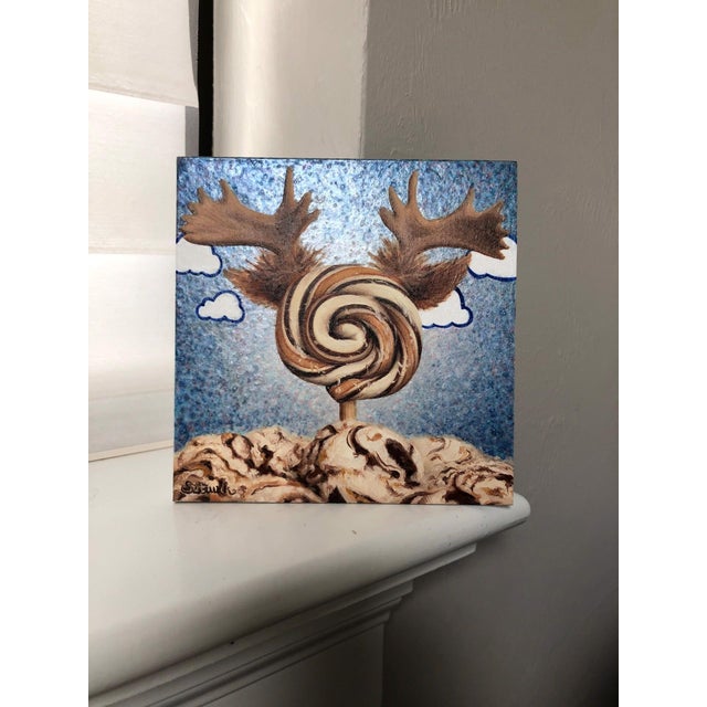 This whimsical artwork features a large, swirled lollipop adorned with moose antlers, set against a playful blue sky...