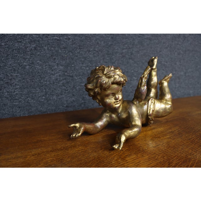 Antique Italian cherub sculpture depicting a reclining winged putto with curly hair and an outstretched pose. The figure...