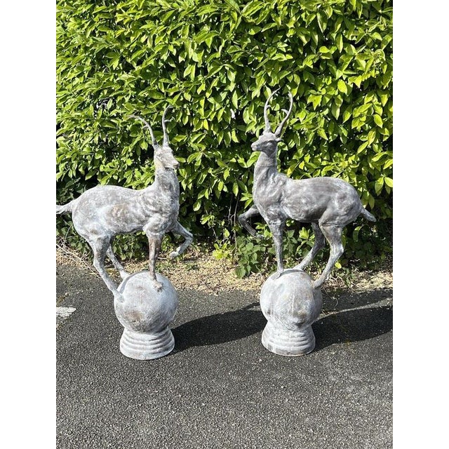 A striking pair of large cast-iron stag and deer garden sculptures, each depicted standing gracefully upon a spherical...