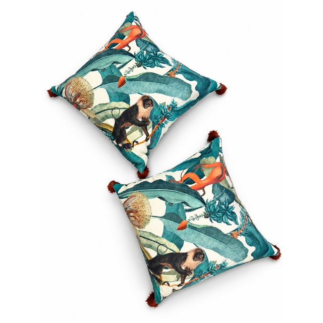 A pair of custom linen pillows featuring a tropical print with playful monkeys, oversized foliage, and vibrant orange...