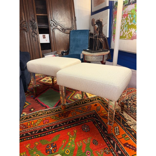 Pair of custom ottomans. Composed of acrylic lucite and upholstered in a woven cream colored bucle style fabric. The...