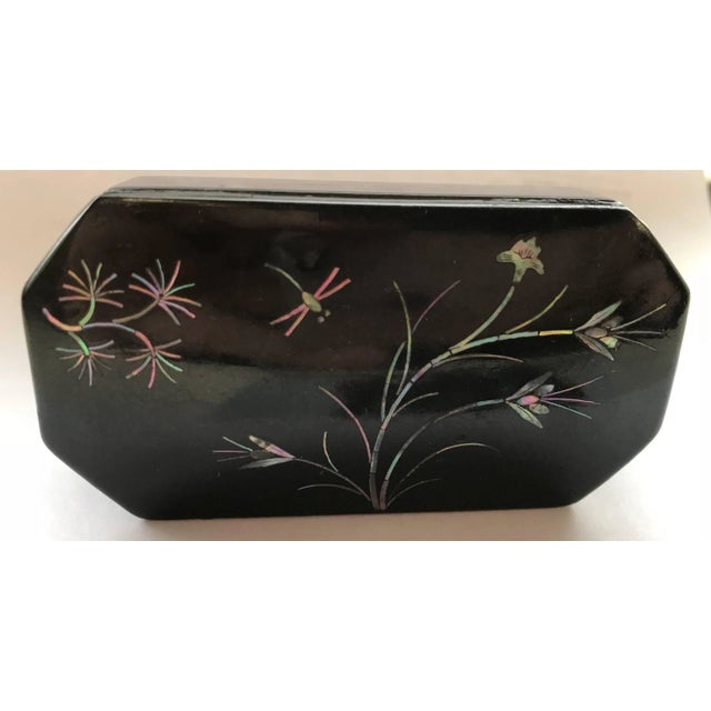 A dragonfly is flying amongst the inlaid mother-of-pearl flowers on this Asian black lacquer snuff box. It has angled...