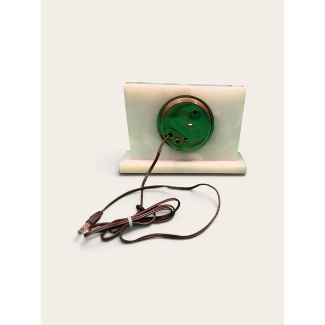A mid-century electric mantel clock cut from white onyx, its soft veining lifted by vertical brass inlay and a round gold-...