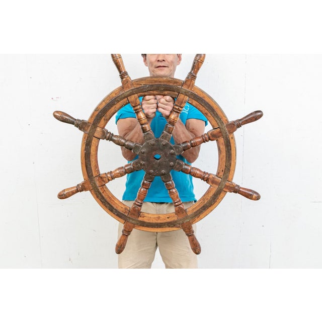 An antique solid mahogany ship’s wheel with lovely patina, an iron core axel, iron bound circular reinforcement strap, and...