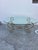 Vintage Hollywood Regency style coffee table featuring a gold-finished wrought iron base with scrollwork and an oval...