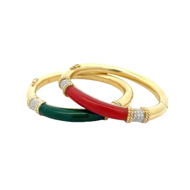 A striking estate pair of hinged bangle bracelets crafted in 18K yellow gold, each showcasing a bold and colorful gemstone...