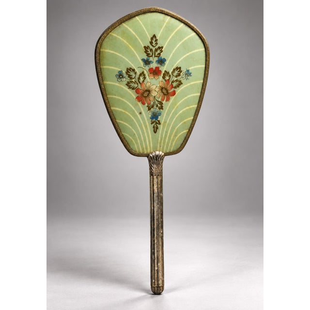This exquisite vanity hand mirror features an elongated, shield-shaped glass pane set within a gilded brass frame with...