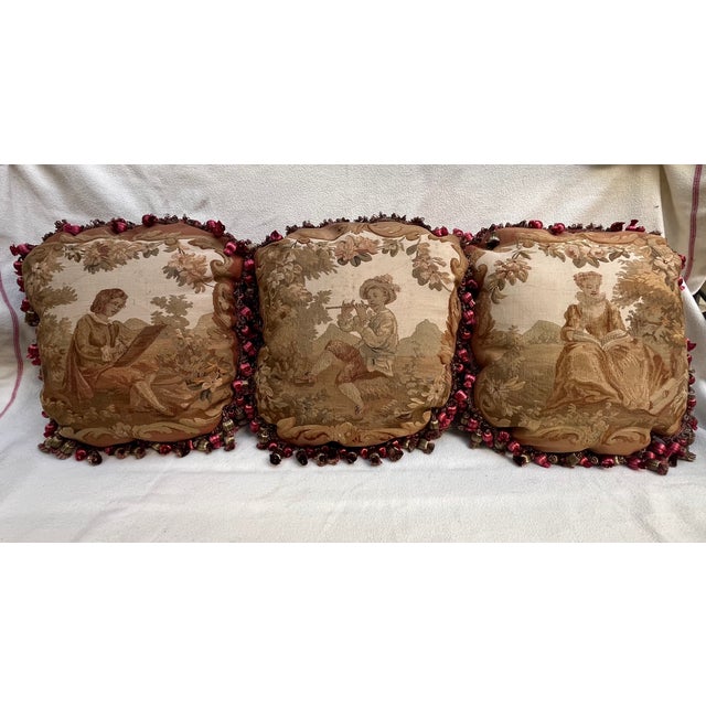 Set of three 19th-century decorative wool and silk pillows featuring charming pastoral scenes in soft, muted tones. Each...