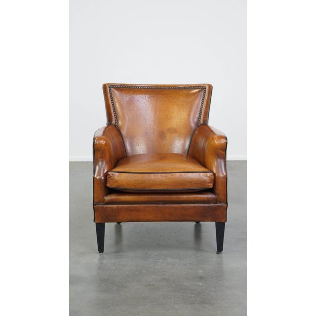 This subtle cognac-colored sheep leather armchair with a nice design and finish with black piping and decorative nails. A...