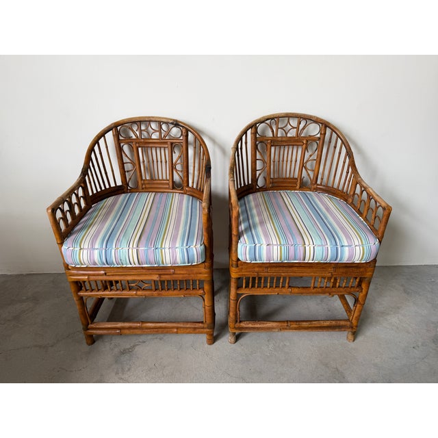 A charming pair of vintage Brighton Pavilion style bamboo and rattan chairs featuring gracefully curved barrel backs and a...