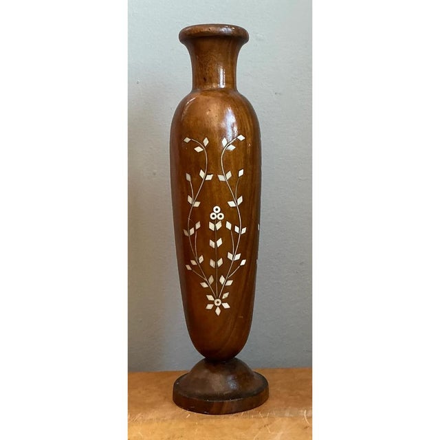 Crafted from rich, warmly patinated wood, this vintage vase showcases intricate mother of pearl inlay forming delicate...