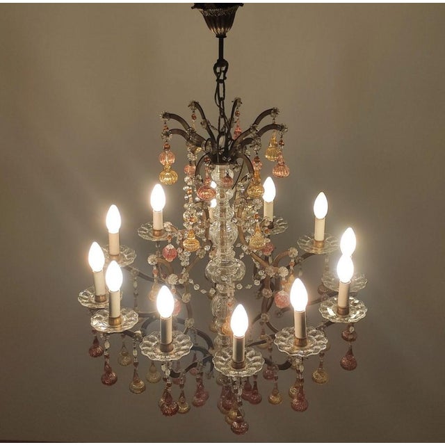 Large 12-light chandelier with a gilded iron frame and warmly colored blown glass pendants. The lamp's design and...