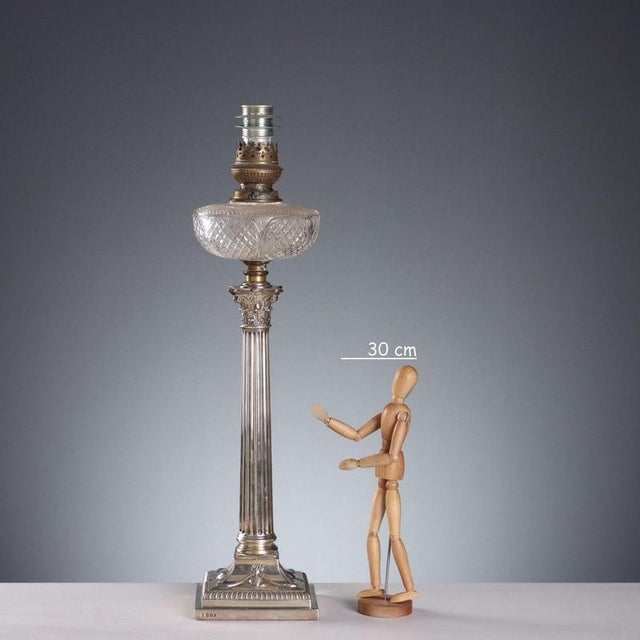 Embossed and chased sterling silver lamp in the shape of a Corinthian column topped with a glass ball. Base decorated with...