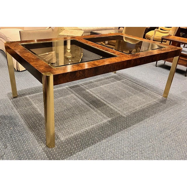 A striking 1970s dining table by Century Furniture, featuring richly figured burl wood paired with sleek brass legs for a...