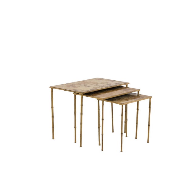 Maison Bagues. Set of three nesting tables in gilded brass and églomisé glass. French work realized in the 1970s. This...