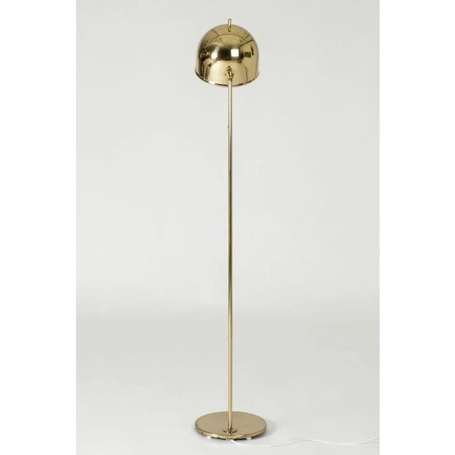 Brass floor lamp from Bergboms, with a sleek, rounded design topped off with a little tip at the top of the lampshade....