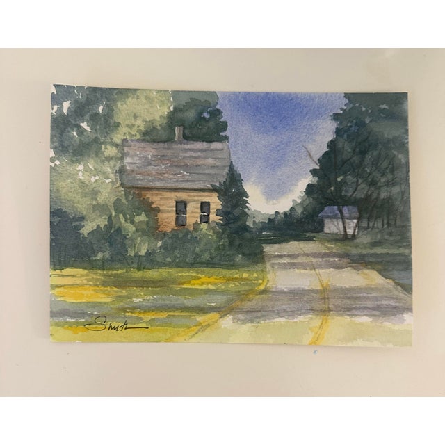 A serene watercolor capturing a quiet country road curving past a small cottage nestled in lush greenery. Soft washes of...