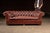 Classic three-seat Chesterfield sofa upholstered in deep burgundy leather with hand-tufted cushioning and decorative brass...