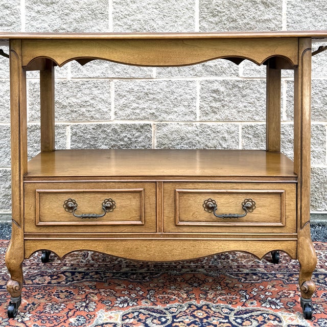 A vintage French Louis XV blond walnut drop leaf serving cart or bar cart having a shaped top and apron over an open...