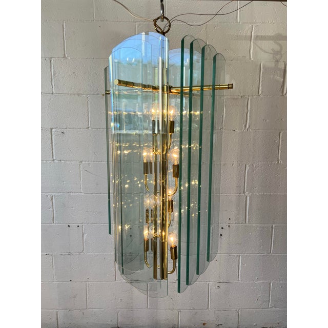 A striking modernist chandelier featuring sixteen clear beveled glass panels with a subtle green tint along their...