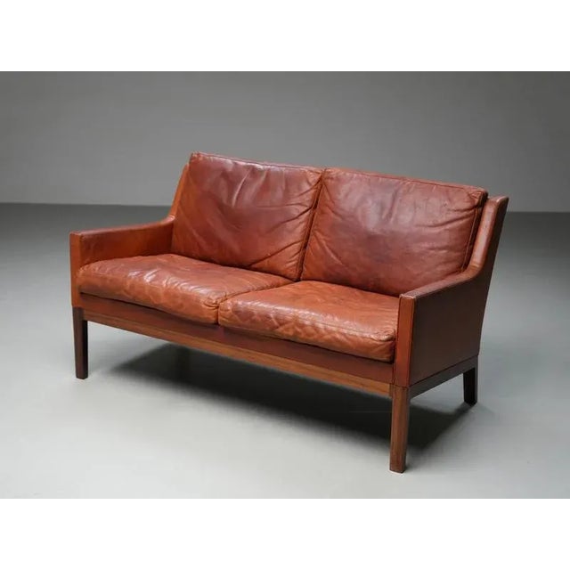 A rare and characterful loveseat by Danish designer Kai Lyngfeldt Larsen, upholstered in its original cognac leather. The...