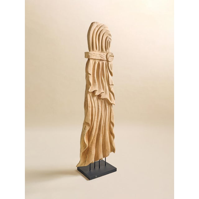 This vintage carved teak sculpture features an elongated carved form set on a black metal base. The draped, fabric-like...