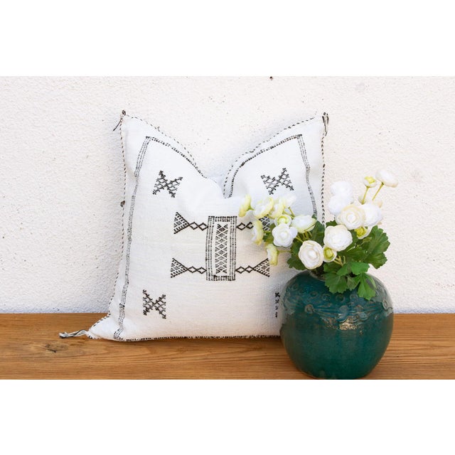 Two crossed-X motifs flank a central bowtie medallion on this handcrafted Moroccan cactus silk pillow, hand-stitched in...