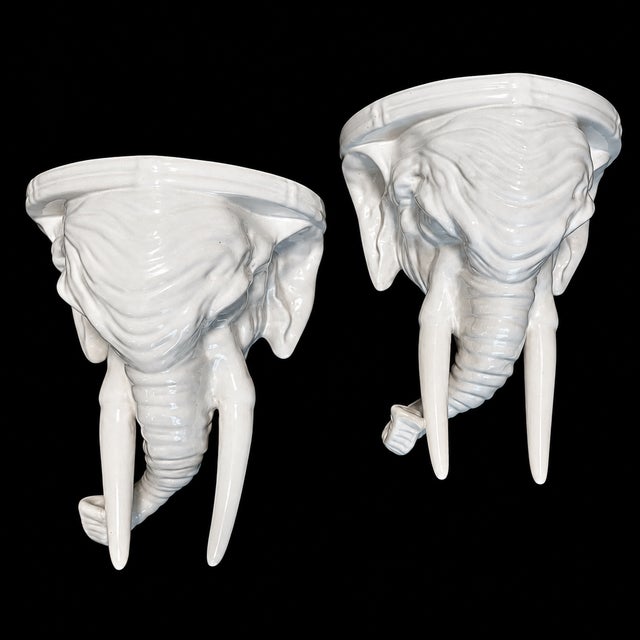 Offered is a pair of Mid Century white glazed elephants head wall brackets. On their back side they have a stretch of wire...