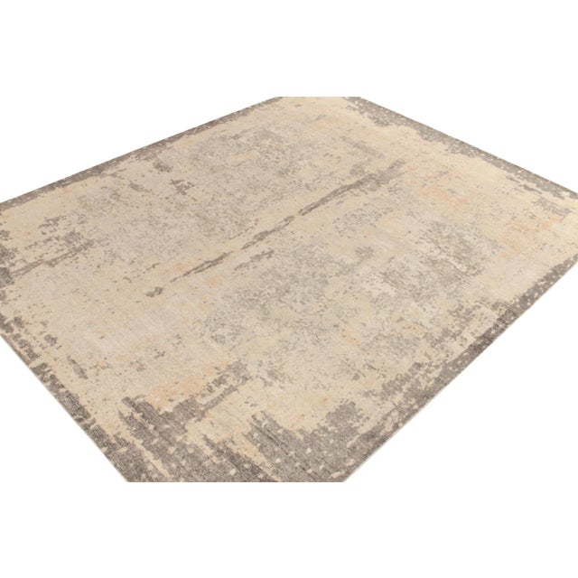 From Rug & Kilim’s Homage collection, a 9x12 distressed style abstract rug in silver/gray, cream & beige colorways playing...