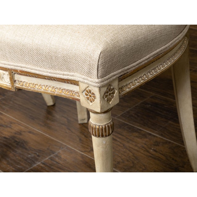 A pair of English Neoclassical style painted wood side chairs from the early 20th century with parcel gilt décor and...