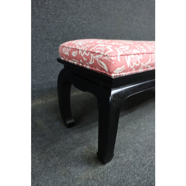 Asian-style bench featuring a black lacquered wood base with gently curved legs. The seat is upholstered in a pink...