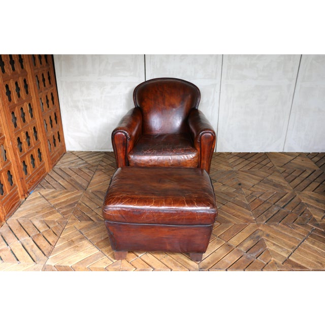 Beautiful vintage leather club chair paired with a matching ottoman. Upholstered in rich, distressed leather with a...