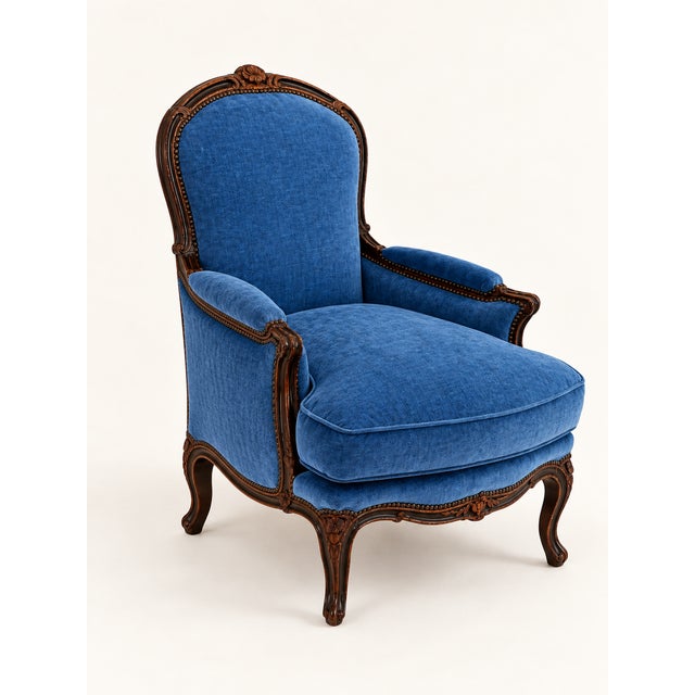A beautifully shaped armchair featuring a carved wood frame, curved arms, and richly textured blue chenille upholstery....