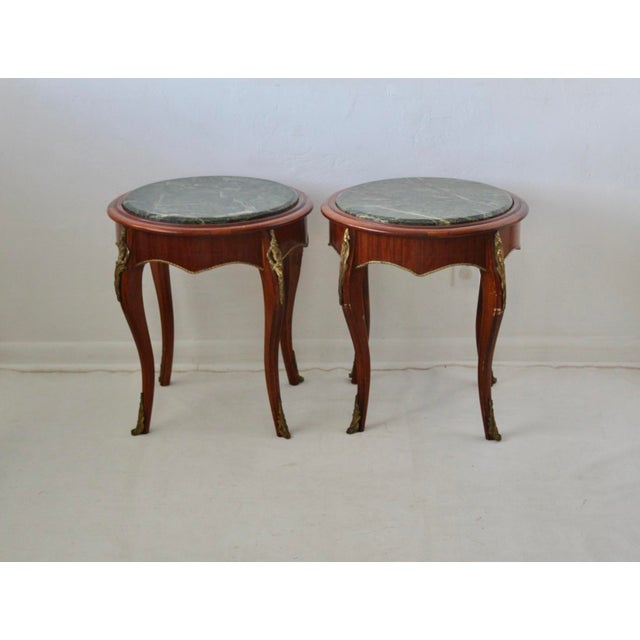 These French Louis XV-style occasional tables feature circular green marble tops, wood solids and veneers, with brass...