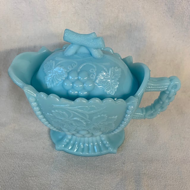 The item is an antique Westmoreland blue milk glass grape and cherry patterned creamer pitcher featuring a matching lid...