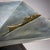 Square metal centerpiece raised on a pyramidal base, featuring a jagged decorative element along the rim, executed in a...