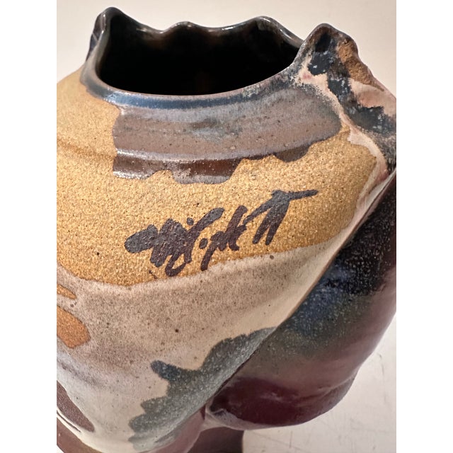 This striking handcrafted ceramic vessel features a sculptural, faceted form with an irregular rim and an oval mouth...