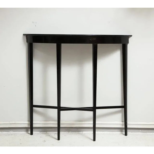 A Bespoke ebonized demilune console on tapered legs can be made in different sizes, materials and finishes.